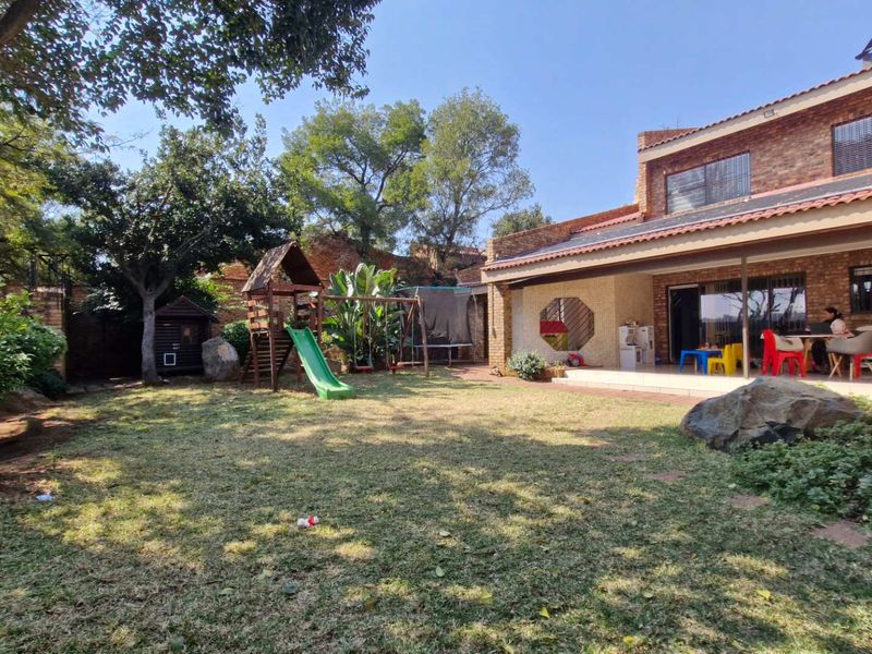 Spacious rear garden featuring a large lawn, mature trees, and a covered patio area with brick exterior finishes and solar panels.