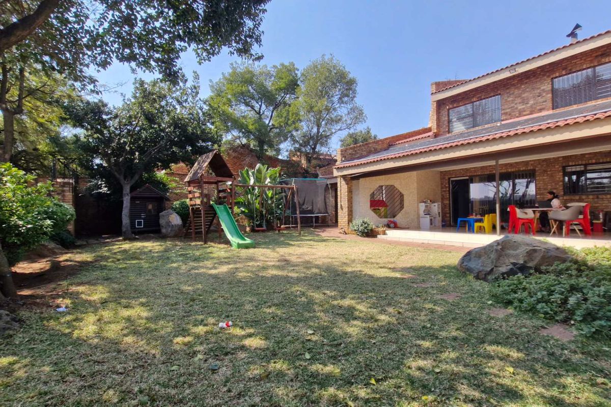 Spacious rear garden featuring a large lawn, mature trees, and a covered patio area with brick exterior finishes and solar panels.