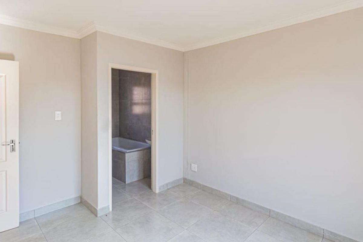 A bright, empty bedroom featuring neutral tiled flooring and a doorway leading to an adjoining bathroom with tiled finishes.