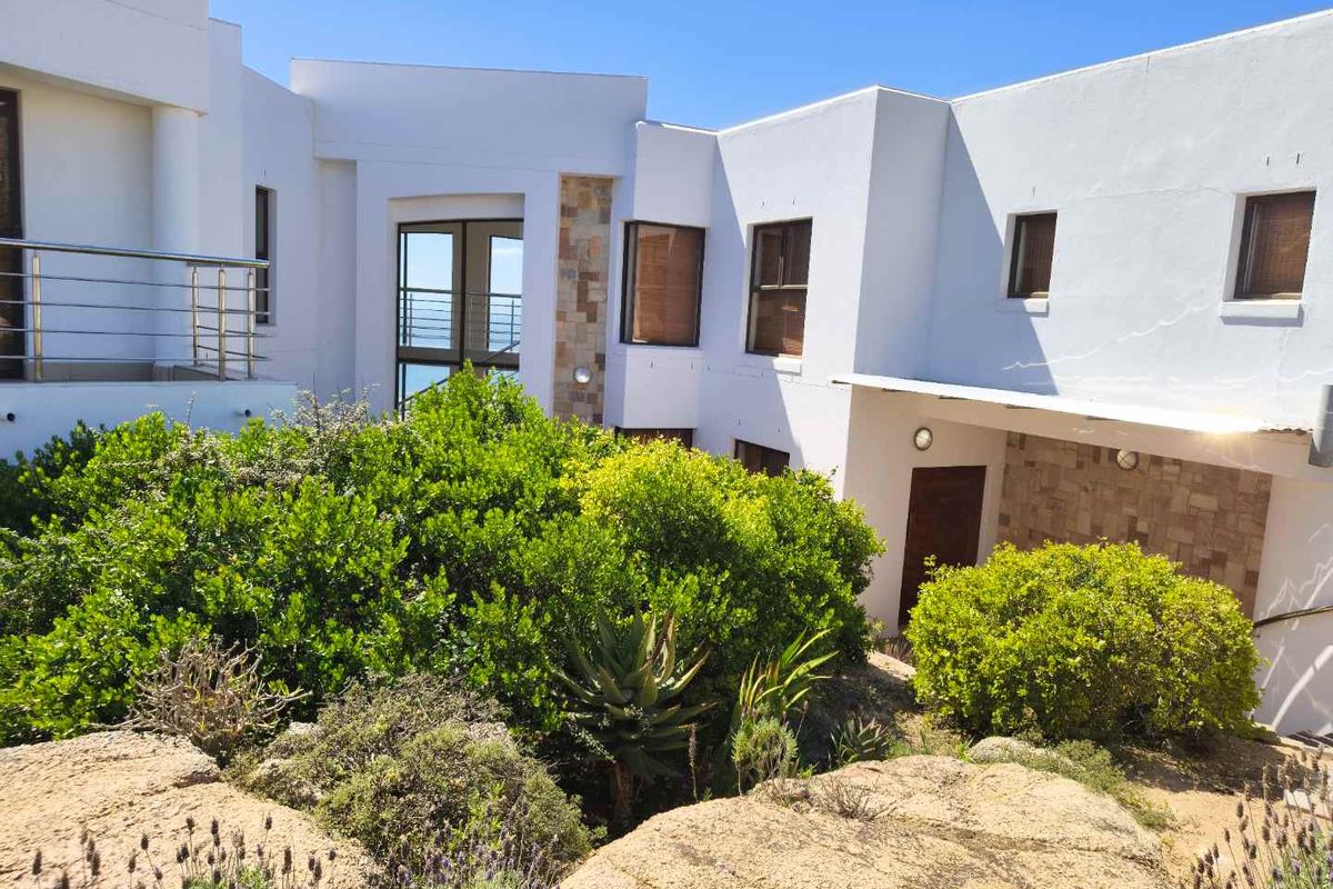 Rear elevation of a modern multi-level home featuring white rendered walls, stone cladding accents, and a stainless steel balcony railing.