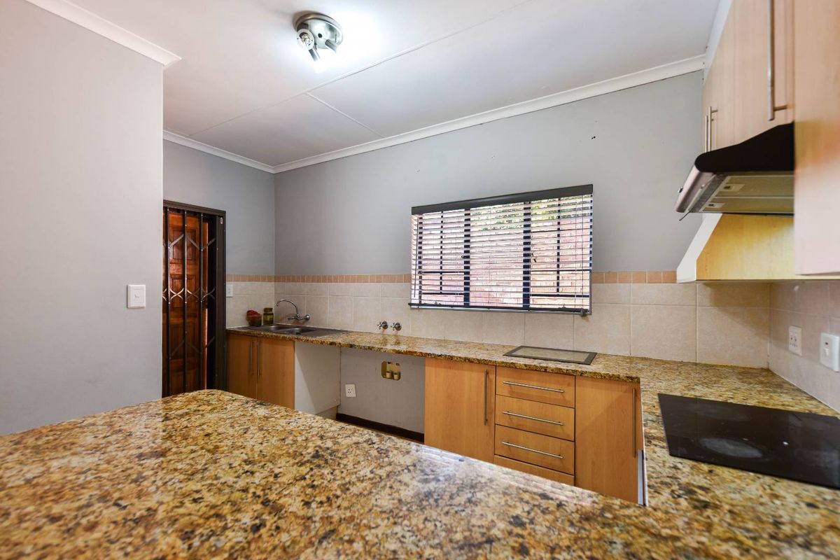 A functional kitchen featuring granite countertops, built-in wooden cabinetry, an electric hob with extractor fan, and a tiled backsplash.