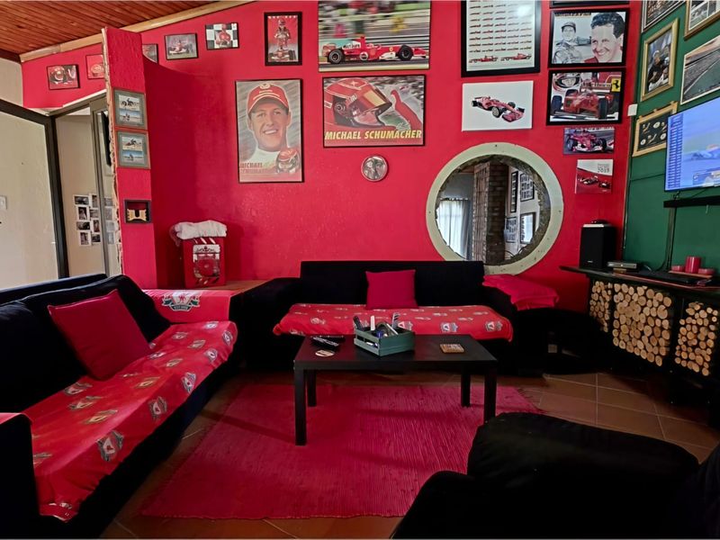 A living room featuring a timber ceiling, tiled flooring, and a distinctive circular porthole window, currently styled with a bold red and black theme.
