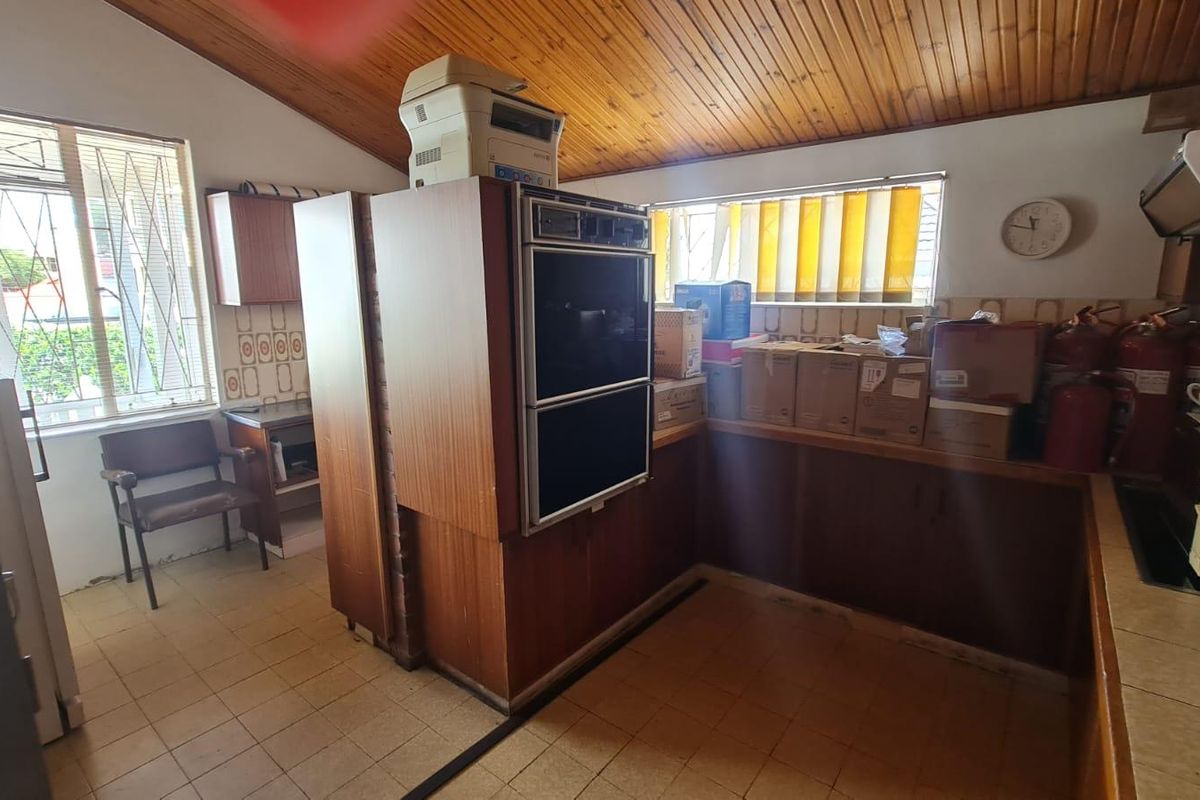 A dated office kitchen area featuring wood-paneled vaulted ceilings, built-in double ovens, and tiled flooring, requiring modernization to improve functionality and aesthetic appeal.