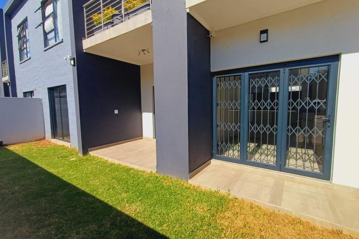 Rear view of the townhouse featuring a covered patio, tiled flooring, and a small private garden area with secure access.