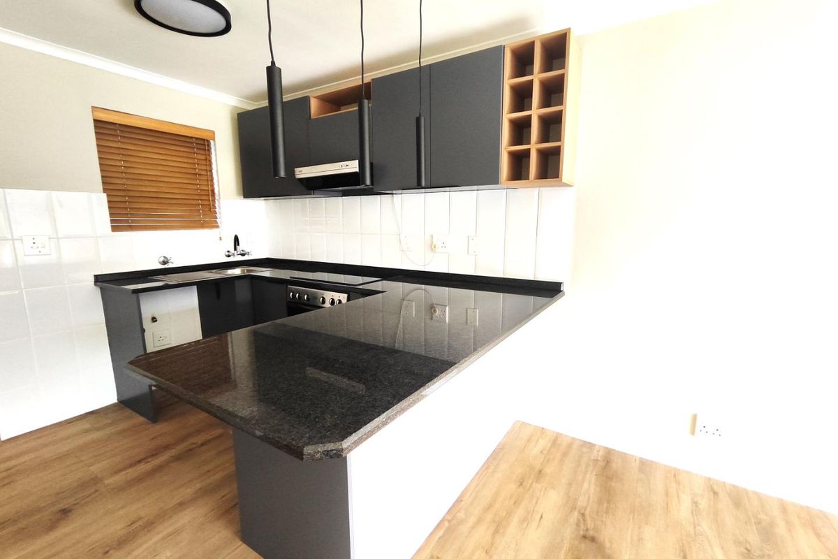 Modern kitchen featuring dark cabinetry, granite countertops, a breakfast bar, tiled backsplash, and integrated extractor fan, set against light wood-look flooring.