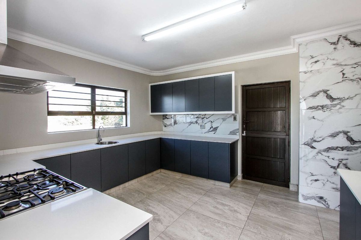 Modern kitchen featuring dark cabinetry, stone countertops, marble-look splashback, integrated gas hob, and stainless steel extractor fan.