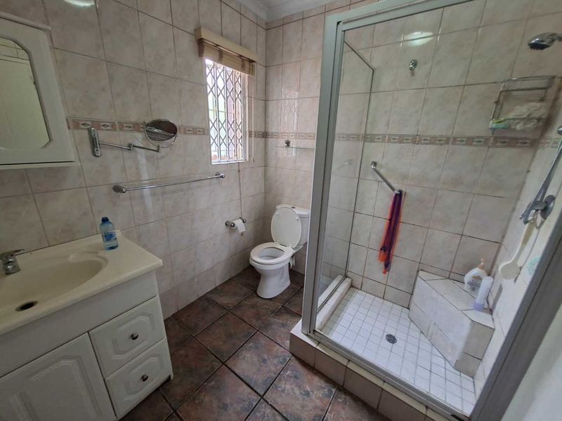 A functional bathroom featuring a vanity cabinet, toilet, and a glass-enclosed shower with tiled walls and flooring.