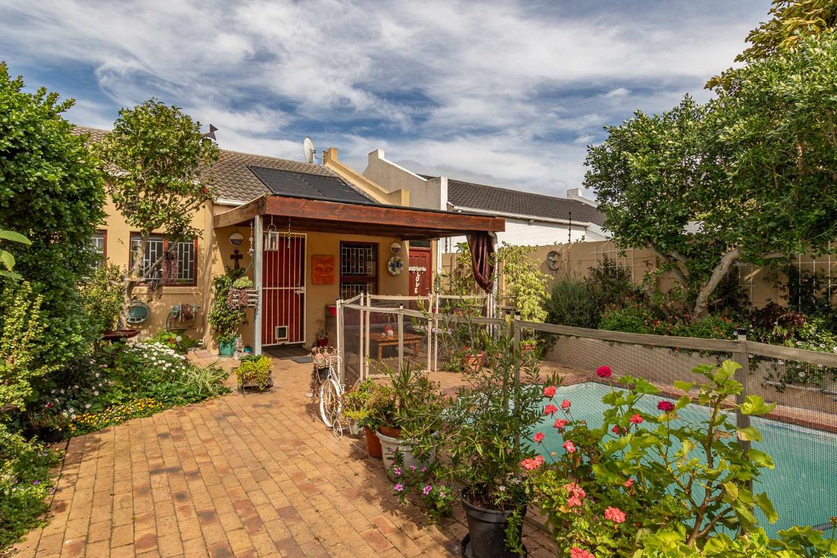 Rear exterior view featuring a paved patio area, a swimming pool with a safety net, and a covered outdoor space with solar panels.