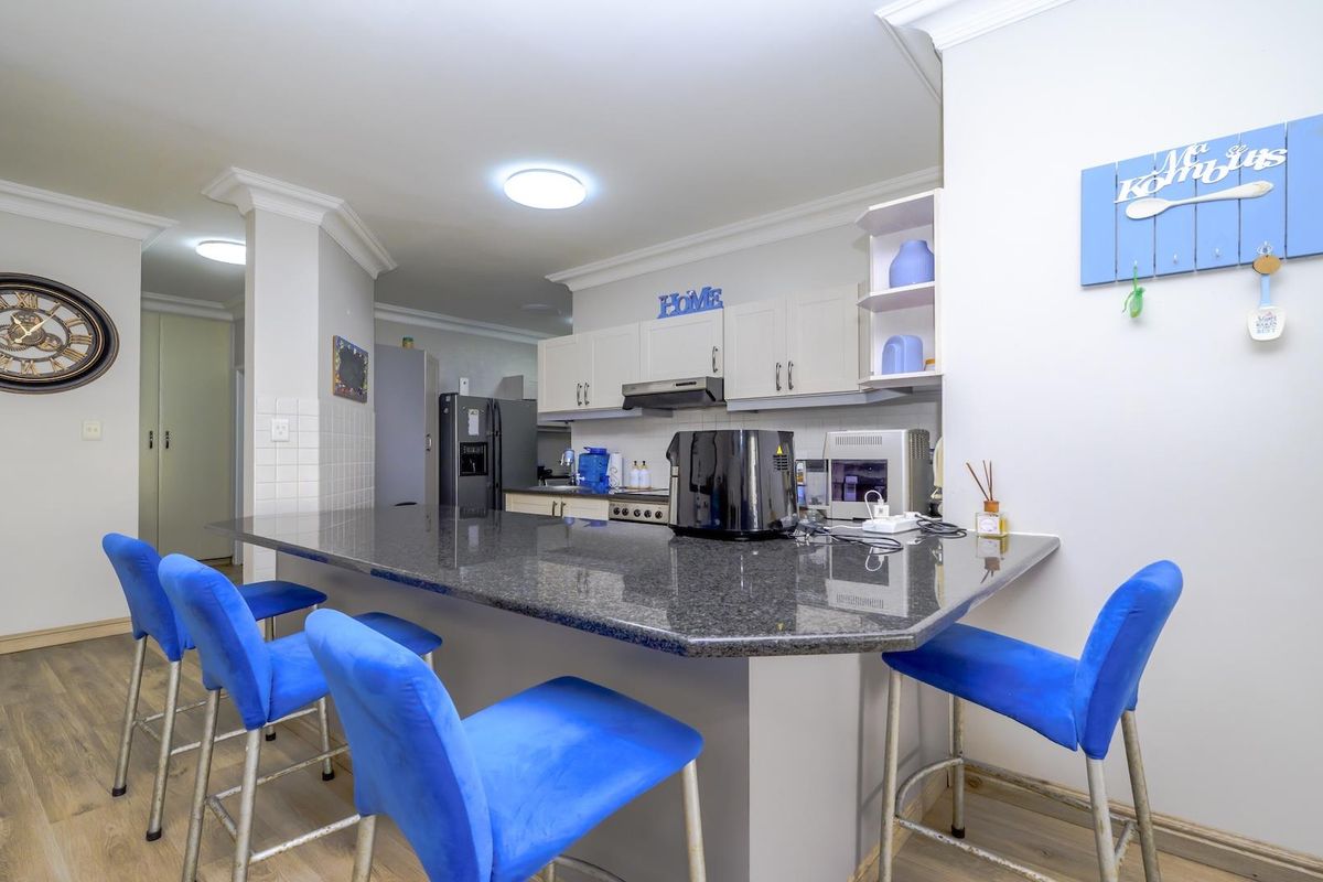 A functional kitchen featuring a large granite breakfast bar, ample built-in cabinetry, and modern laminate flooring, providing a practical space for cooking and dining.