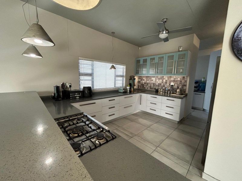 Modern kitchen featuring stone countertops, a gas hob, ample built-in cabinetry, and a decorative tiled backsplash, complemented by contemporary pendant lighting.