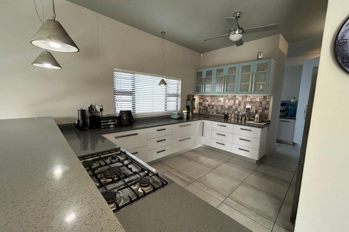 Modern kitchen featuring stone countertops, a gas hob, ample built-in cabinetry, and a decorative tiled backsplash, complemented by contemporary pendant lighting.