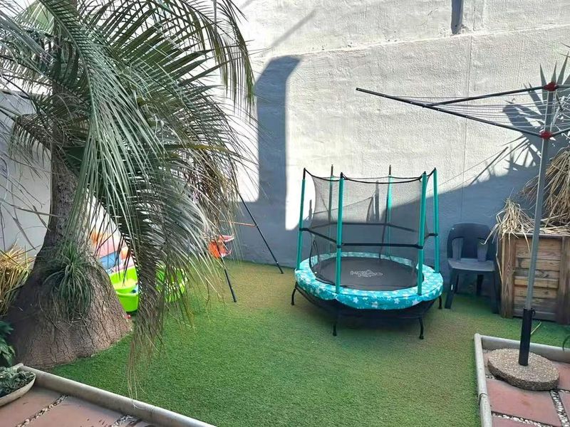 A compact rear courtyard area featuring artificial turf, a boundary wall, and paved edging, suitable for outdoor play or relaxation.