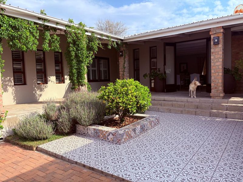 A well-maintained rear patio area featuring decorative patterned tiles, brick pillars, and direct access to the interior through double doors.