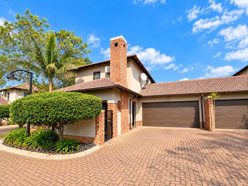 Front exterior view of a townhouse featuring a brick chimney, tiled roof, and a double garage with a paved driveway.