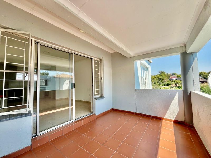 A covered balcony featuring tiled flooring, a sliding glass door with security gate, and an open-air view.