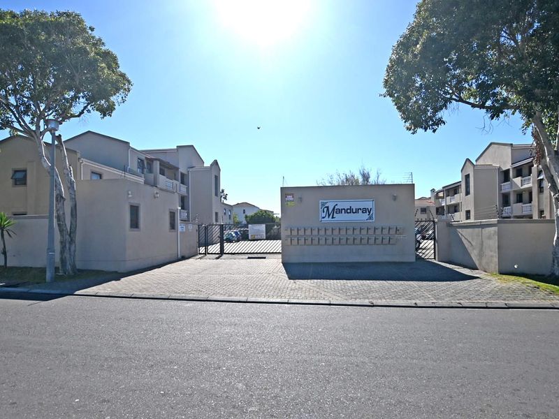 Front entrance view of Manduray apartment complex featuring a paved driveway, secure gated access, perimeter walling, and a bank of post boxes.