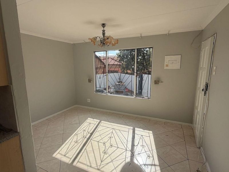 An empty living area featuring tiled flooring, a window with security bars, and a central ceiling light fixture.
