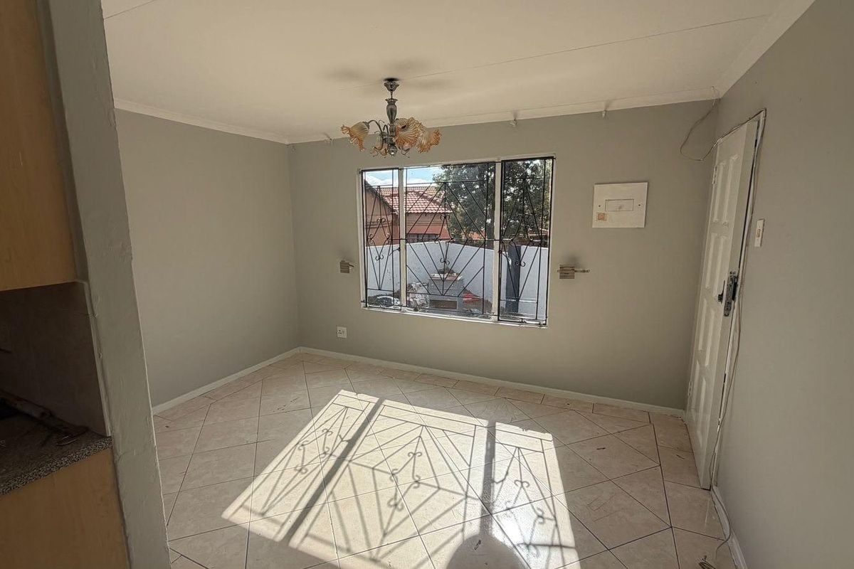 An empty living area featuring tiled flooring, a window with security bars, and a central ceiling light fixture.