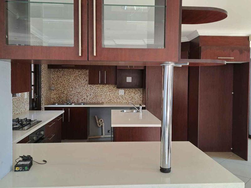 A spacious kitchen featuring dark wood cabinetry, stone countertops, a gas hob, and a breakfast bar, with a mosaic tile backsplash.