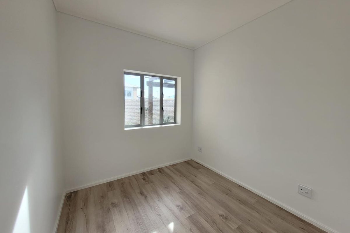 A bright, empty bedroom featuring modern wood-look laminate flooring, neutral white walls, and a window with a view of the rear exterior.
