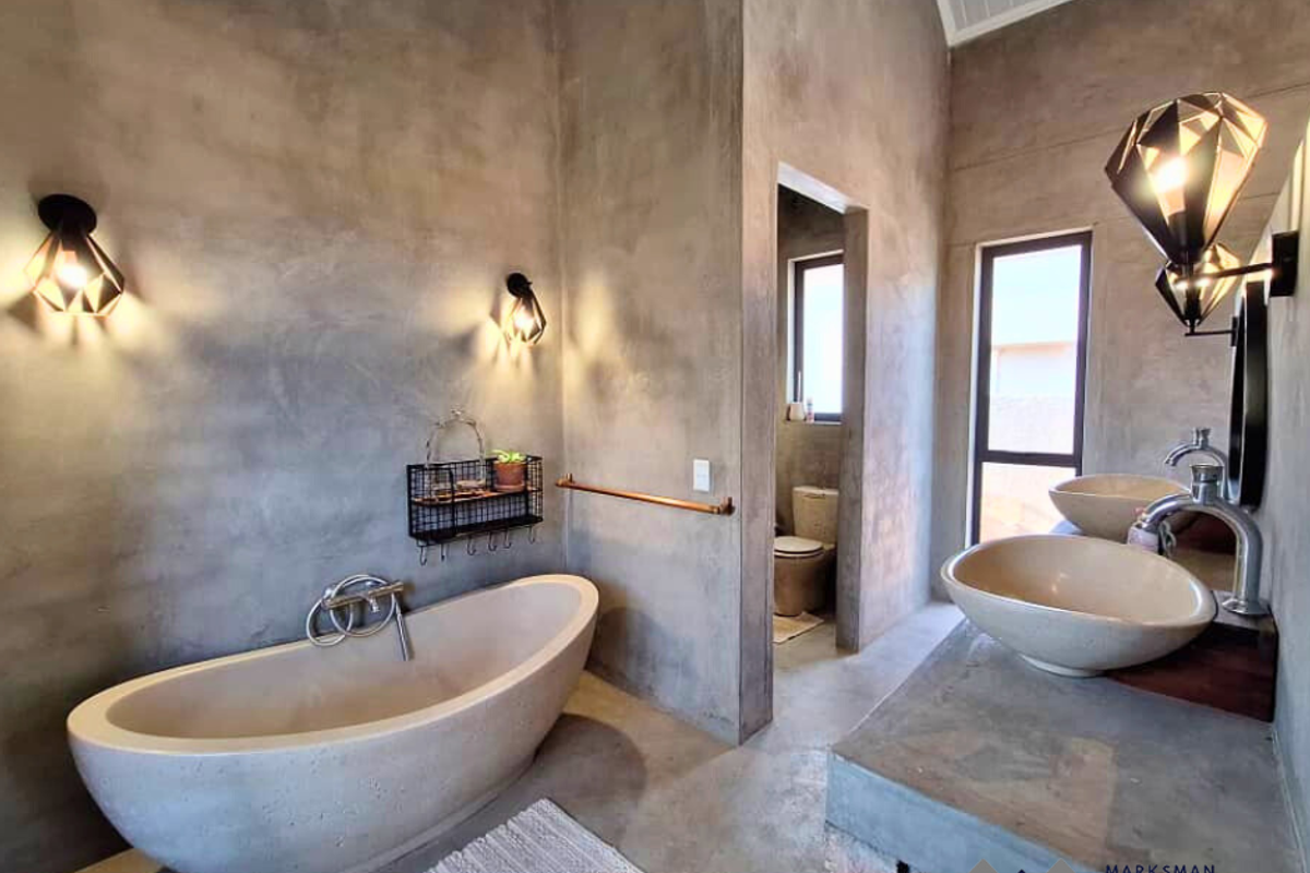 Modern bathroom featuring a freestanding stone bathtub, dual vessel sinks on a concrete vanity, and industrial-style wall lighting with polished concrete finishes.