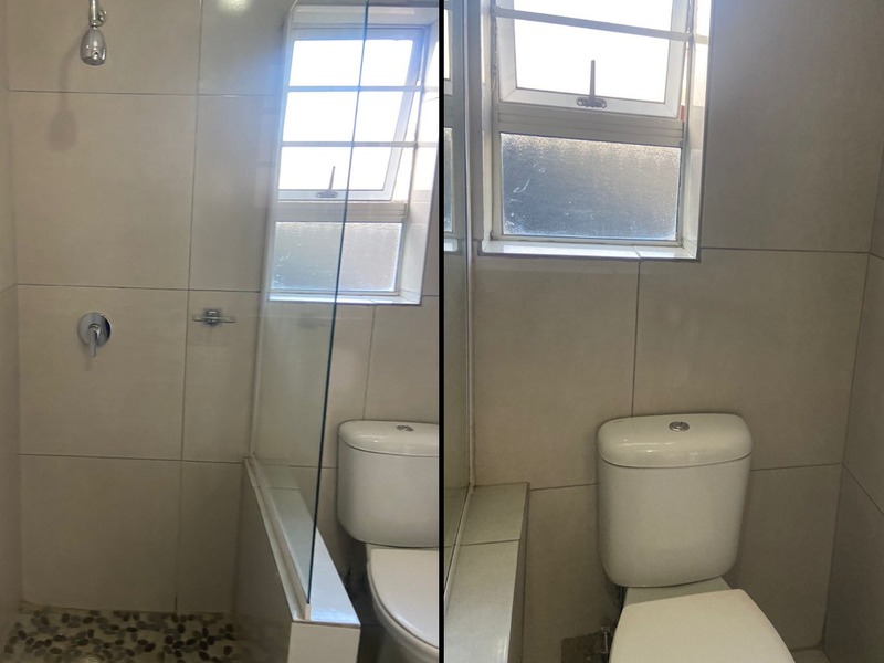A compact bathroom featuring a shower with a pebble floor, glass screen, and a standard toilet with neutral wall tiling.