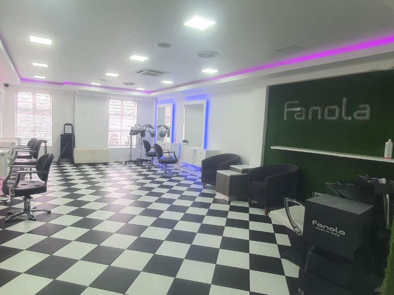 A well-lit commercial salon space featuring checkered flooring, recessed lighting, built-in cabinetry, and a decorative artificial grass wall feature.