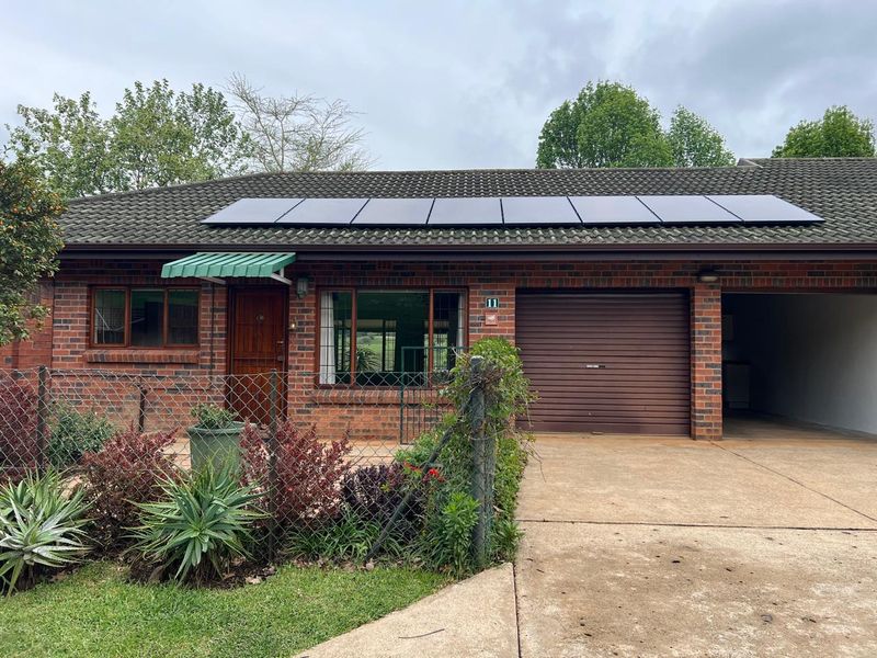 Front elevation of a brick townhouse featuring a tiled roof with solar panels, a roller garage door, and a paved driveway.