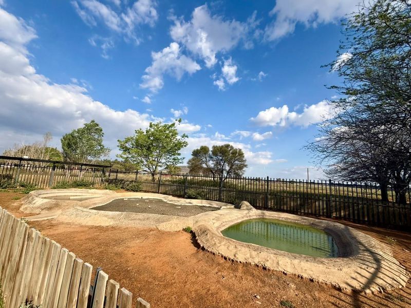 Outdoor area featuring multiple concrete-lined water basins enclosed by metal and wooden perimeter fencing on a farm property.