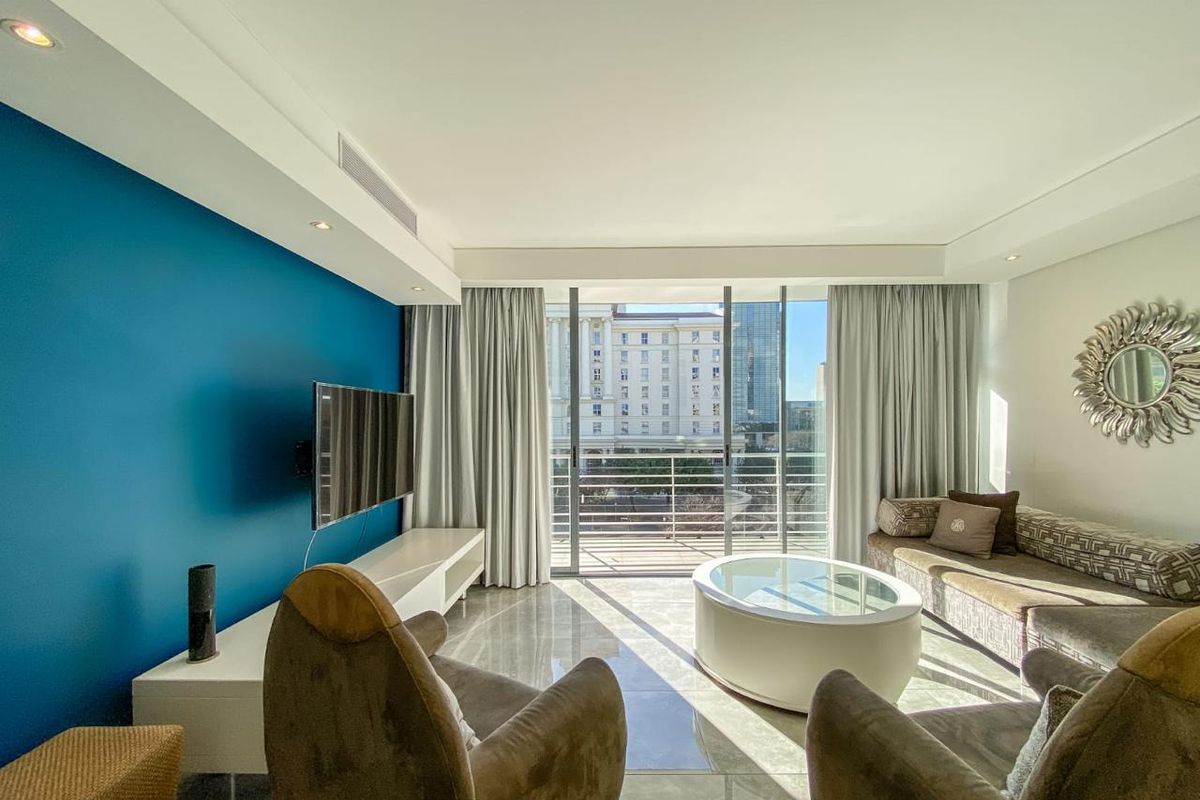 A bright and modern living room featuring tiled floors, recessed lighting, ducted air conditioning, and large sliding glass doors leading to a balcony.