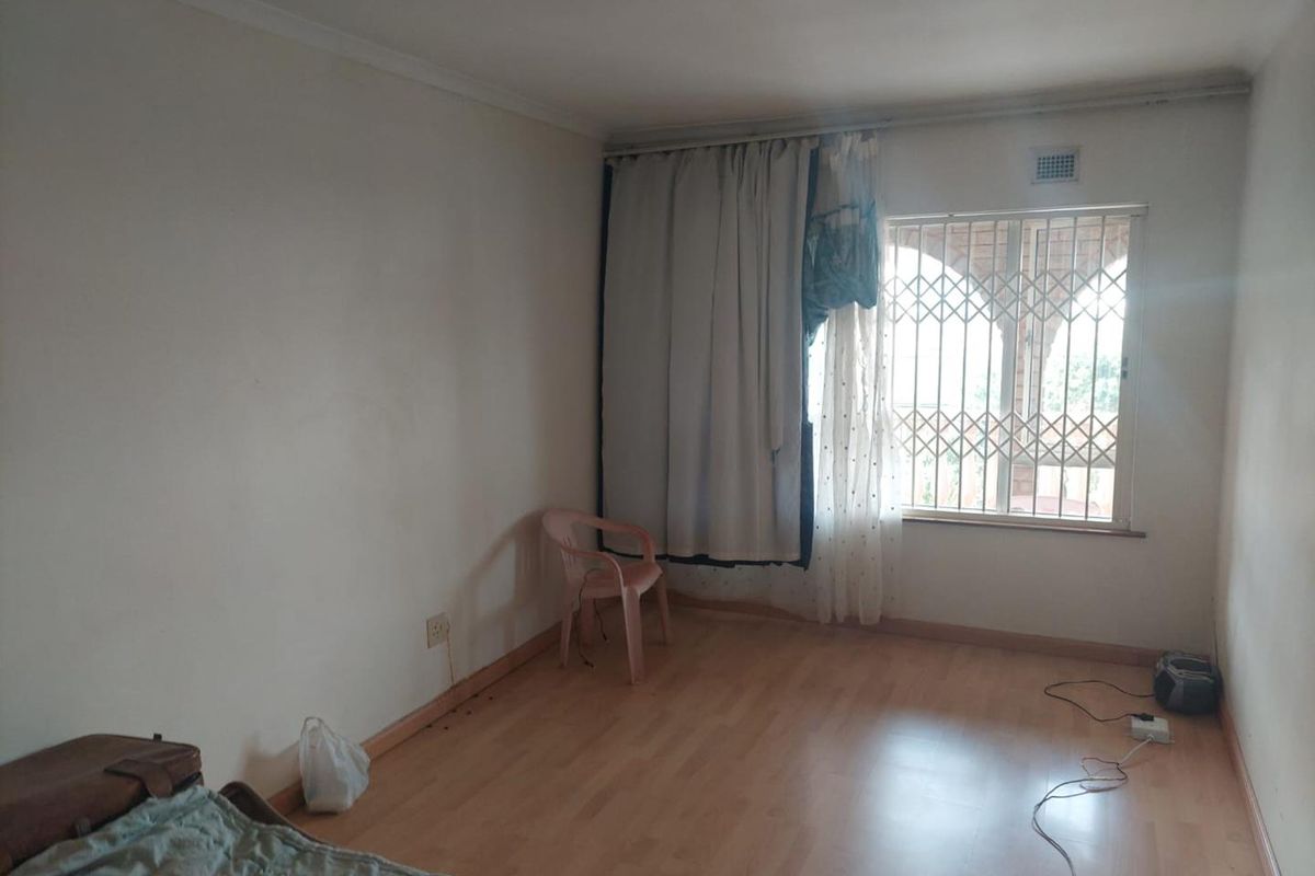 A simple, vacant bedroom featuring laminate flooring and a window fitted with a security gate.