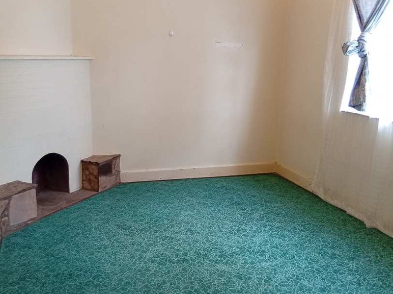 An empty living room featuring a traditional fireplace, vintage ceiling light fixture, and green patterned carpet flooring.