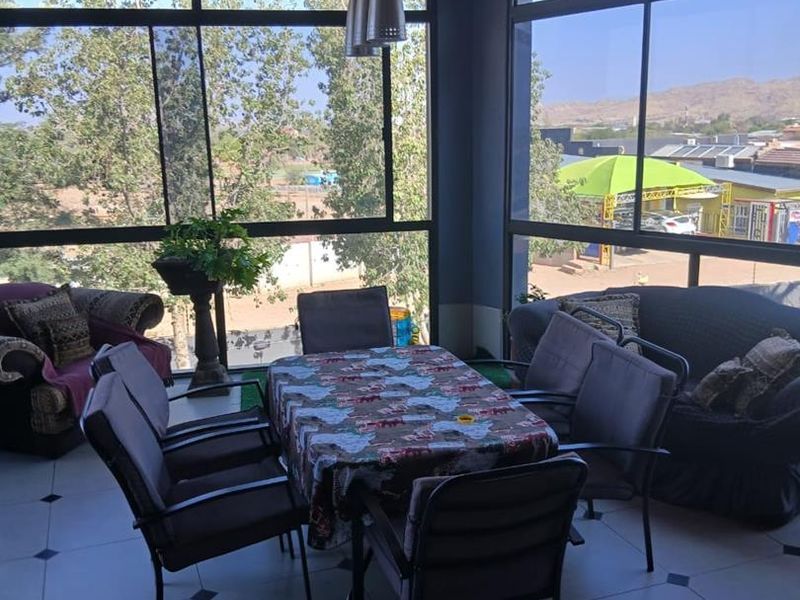 A covered patio area featuring a timber ceiling, large glass windows providing expansive views, and tiled flooring, ideal for outdoor dining and relaxation.