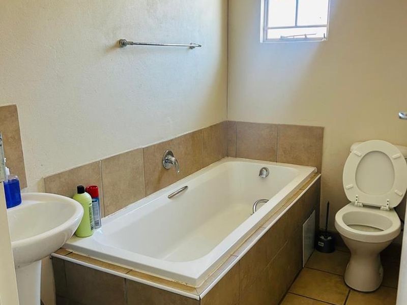 A functional bathroom featuring a built-in bathtub, pedestal basin, and toilet with neutral ceramic tiling throughout.