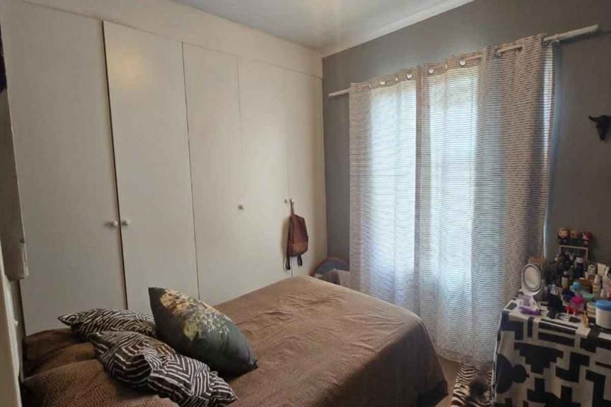 A bedroom featuring built-in cupboards and a window with curtain rails, providing functional storage and natural light.