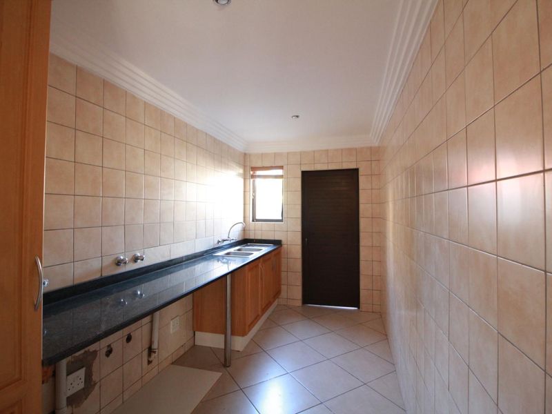 A functional scullery featuring tiled walls, granite countertops, a double sink, and built-in wooden cabinetry with direct access to an exterior door.