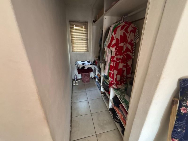 A narrow walk-in closet or dressing area featuring built-in shelving, tiled flooring, and a small window with fitted blinds.