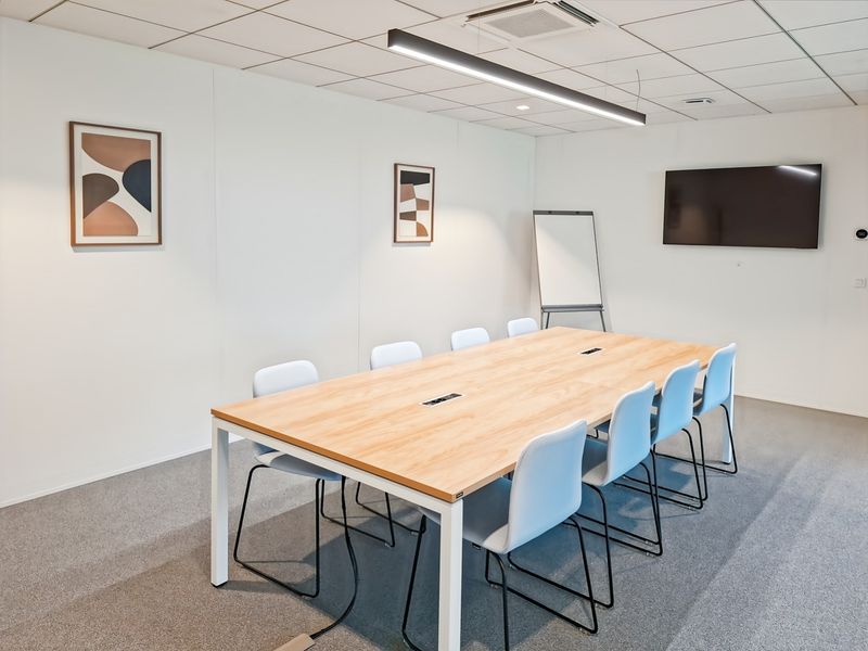 A modern, well-lit office meeting room featuring a large conference table, suspended lighting, and professional carpeted flooring.