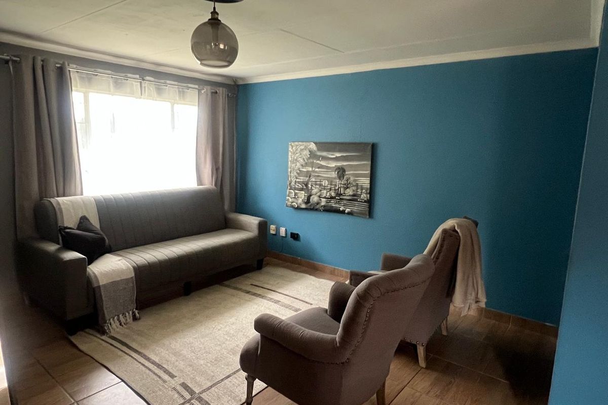 A living room featuring tiled flooring, a large window with curtains, and a bold blue accent wall.