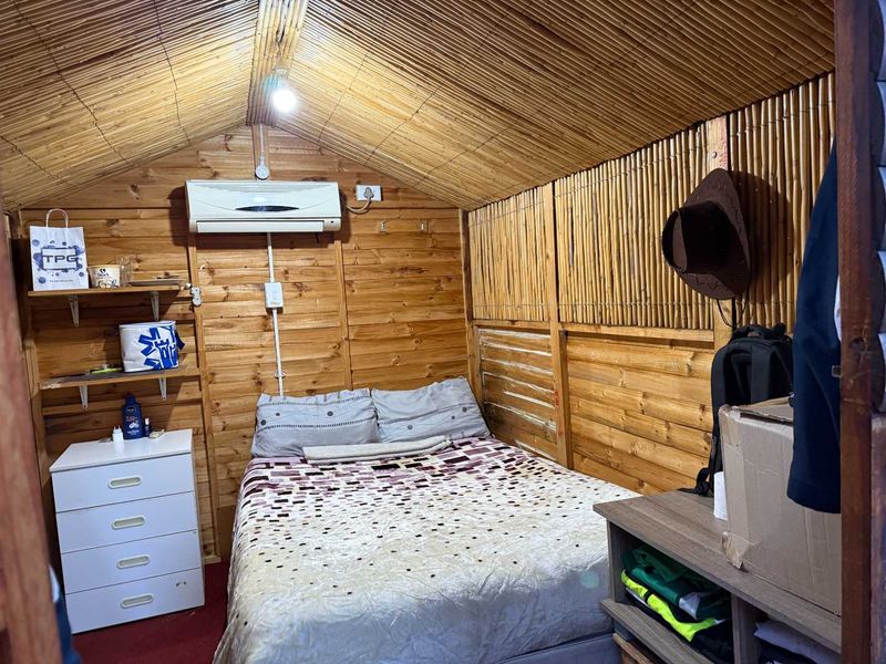 A rustic bedroom featuring timber wall cladding and a bamboo-lined vaulted ceiling, equipped with a wall-mounted air conditioning unit.
