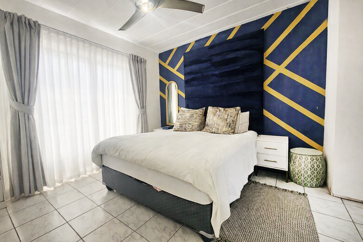 A well-lit bedroom featuring tiled flooring, a ceiling fan, and a large sliding glass door providing access to natural light.
