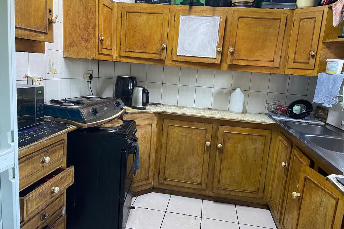 A compact kitchen featuring dated wooden cabinetry, tiled splashbacks, and a functional layout with integrated sink and stove space.