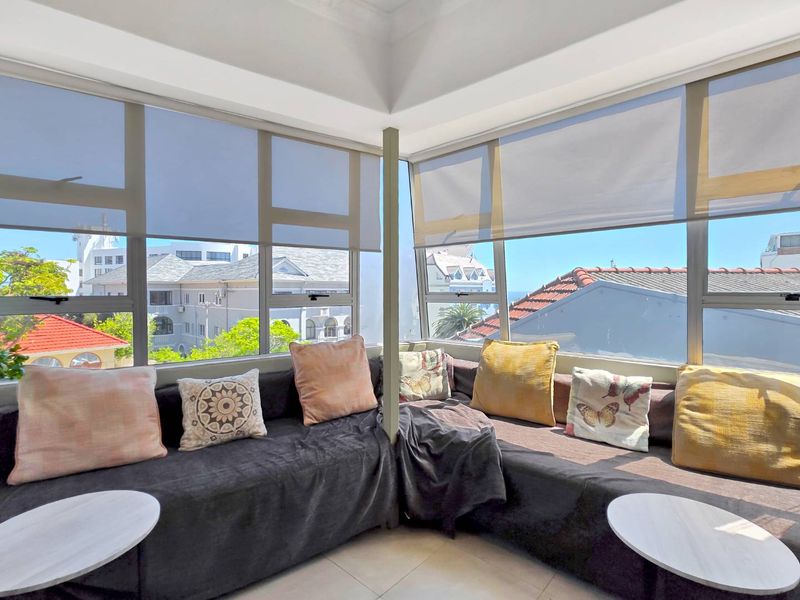 Enclosed balcony or sunroom featuring large windows with roller blinds, tiled flooring, and expansive urban views.
