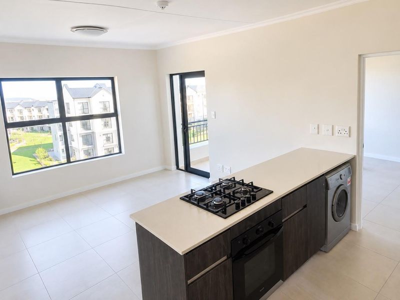 Modern open-plan kitchen and living area featuring sleek dark cabinetry, stone countertops, gas hob, built-in oven, and direct access to a private balcony.