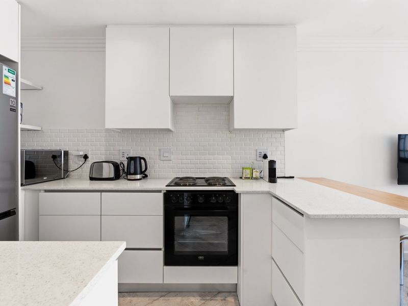 Modern kitchen featuring clean white cabinetry, stone countertops, subway tile backsplash, and integrated appliances, offering a bright and functional cooking space.