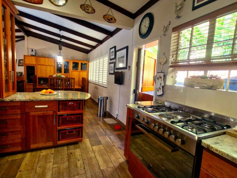 A rustic-style kitchen featuring warm wooden cabinetry, granite countertops, a gas hob, and exposed ceiling beams with wooden flooring throughout.
