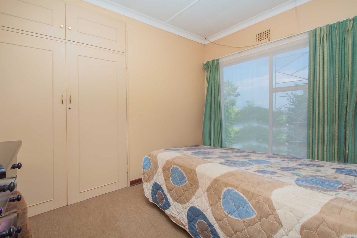 A functional bedroom featuring built-in cupboards, neutral wall finishes, and a large window providing natural light.