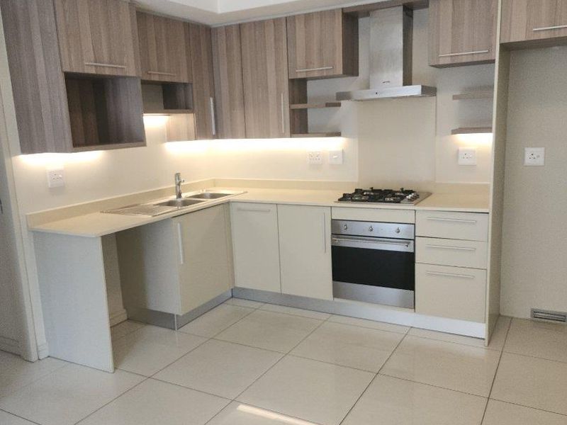 Modern kitchen featuring sleek built-in cabinetry, stone countertops, integrated gas hob, oven, extractor fan, and polished tiled flooring in an open-plan layout.