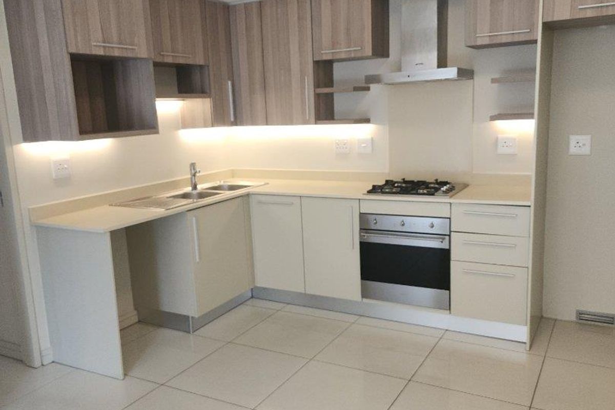 Modern kitchen featuring sleek built-in cabinetry, stone countertops, integrated gas hob, oven, extractor fan, and polished tiled flooring in an open-plan layout.