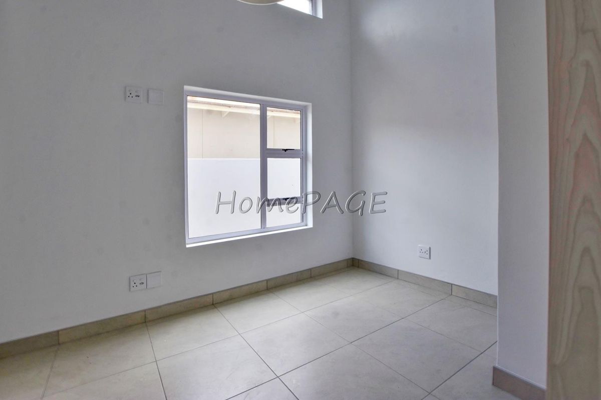 A bright, empty bedroom featuring neutral tiled flooring, white walls, and a window providing natural light.